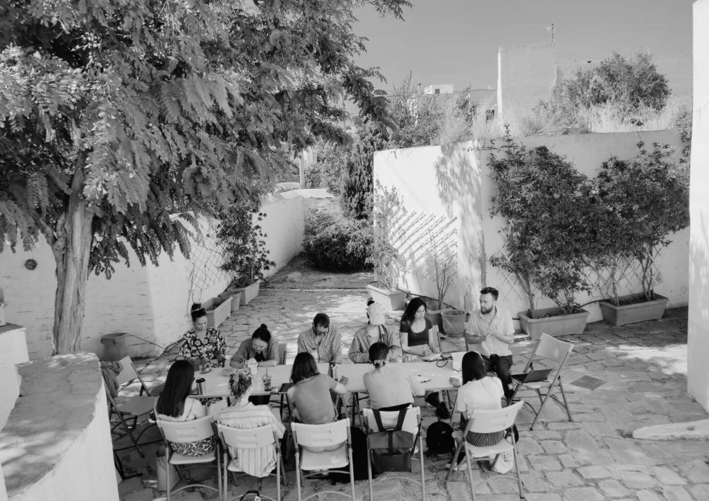 People gathered and working around a large table outdoors on a Greek island