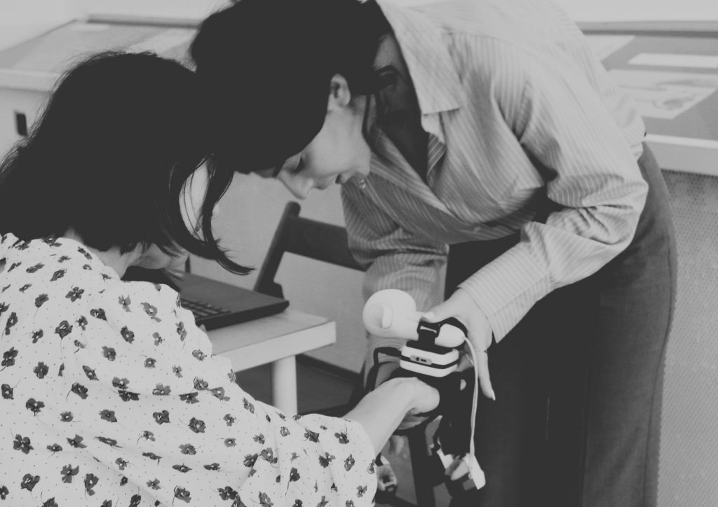 A woman helping another woman wear a haptic glove