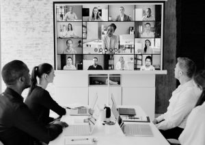 A team around a table watched a zoom meeting onscreen