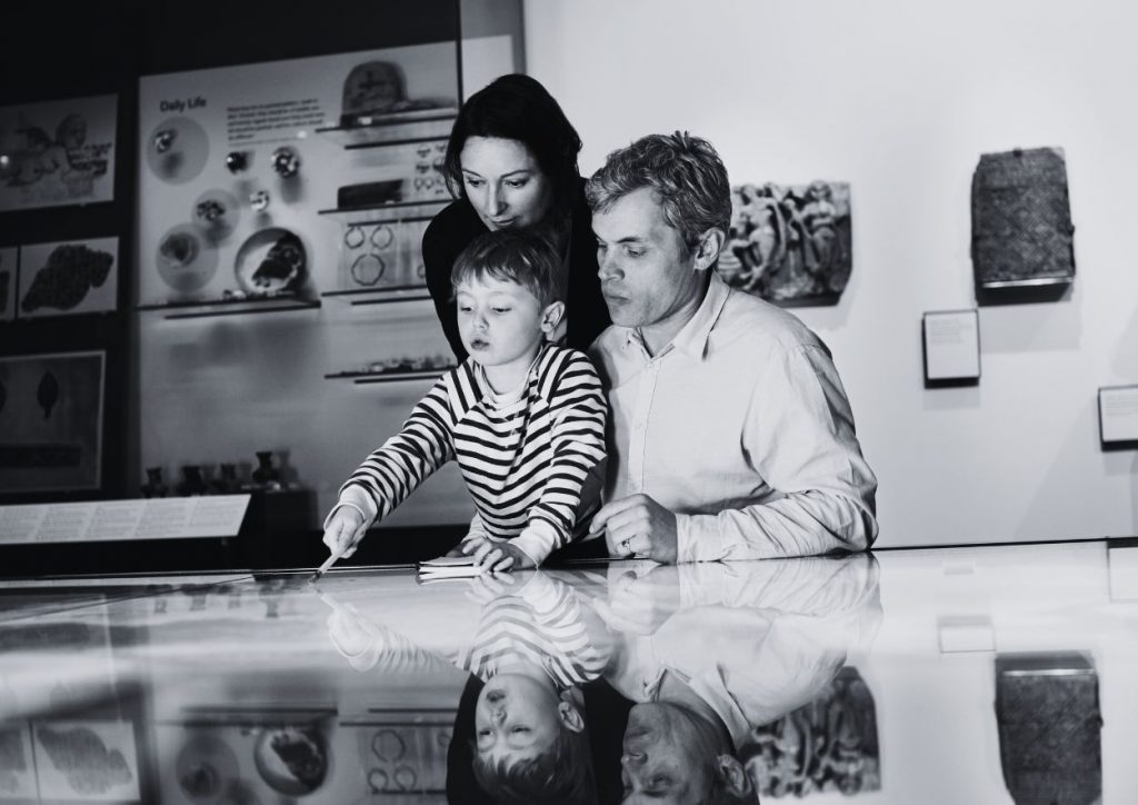 A couple and a child are exploring a screen in what looks like a museum with artefacts behind them